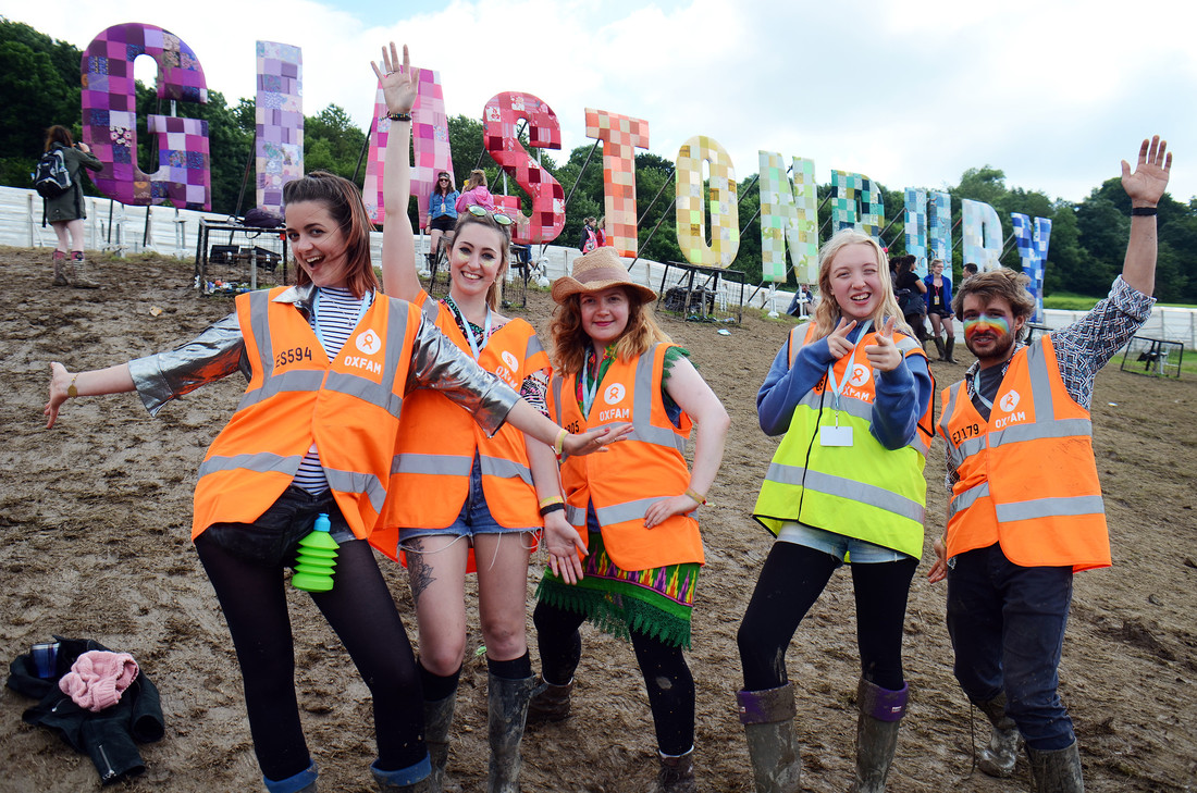 Oxfam stewards smile for the camera in front of the Glastonbury sign.