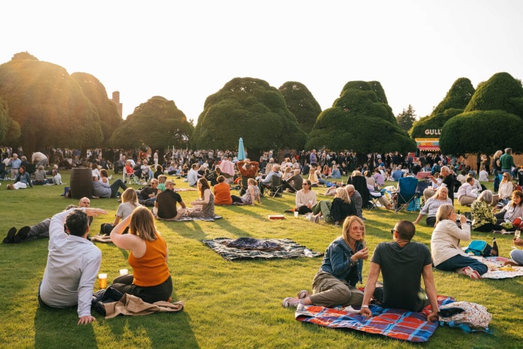 20240618195502 Hampton Court Palace Festival 2024 Sheryl Crow Joshua Atkins JAP 5635 Hampton Court Palace Festival people sitting on grass