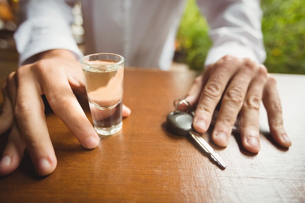man holding glass tequila shot car key bar counter
